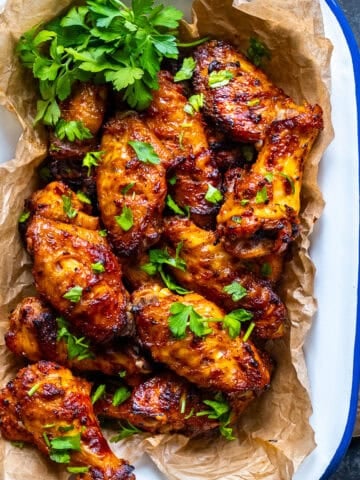 Golden, oven-baked Turkish chicken wings garnished with parsley in a white enamel tray.
