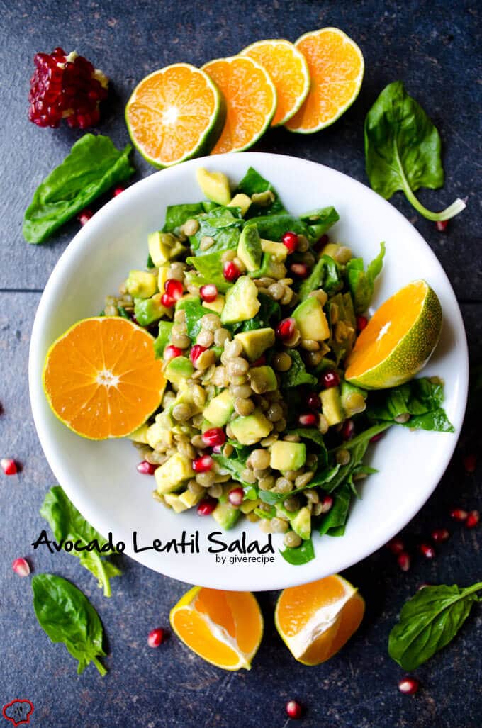 Green Lentil Salad with avocado, mandarin, spinach and pomegranate arils in a white bowl.