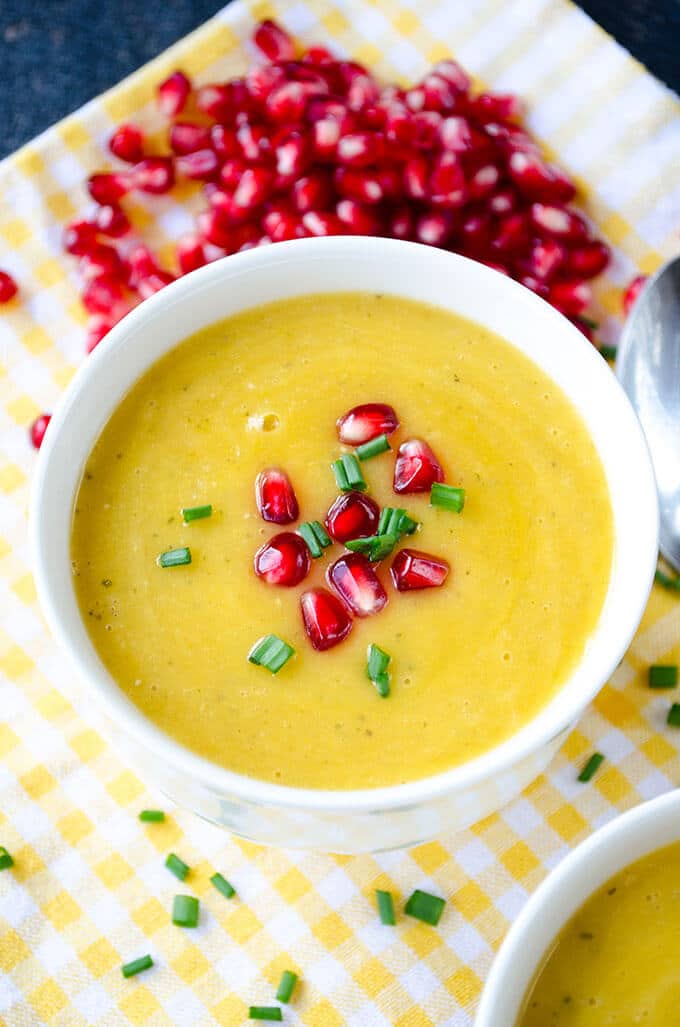 Creamy pumpkin lentil soup garnished with pomegranate arils in a white bowl.