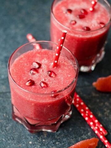 Grapefruit smoothie in glasses garnished with pomegranate arils and red straw.