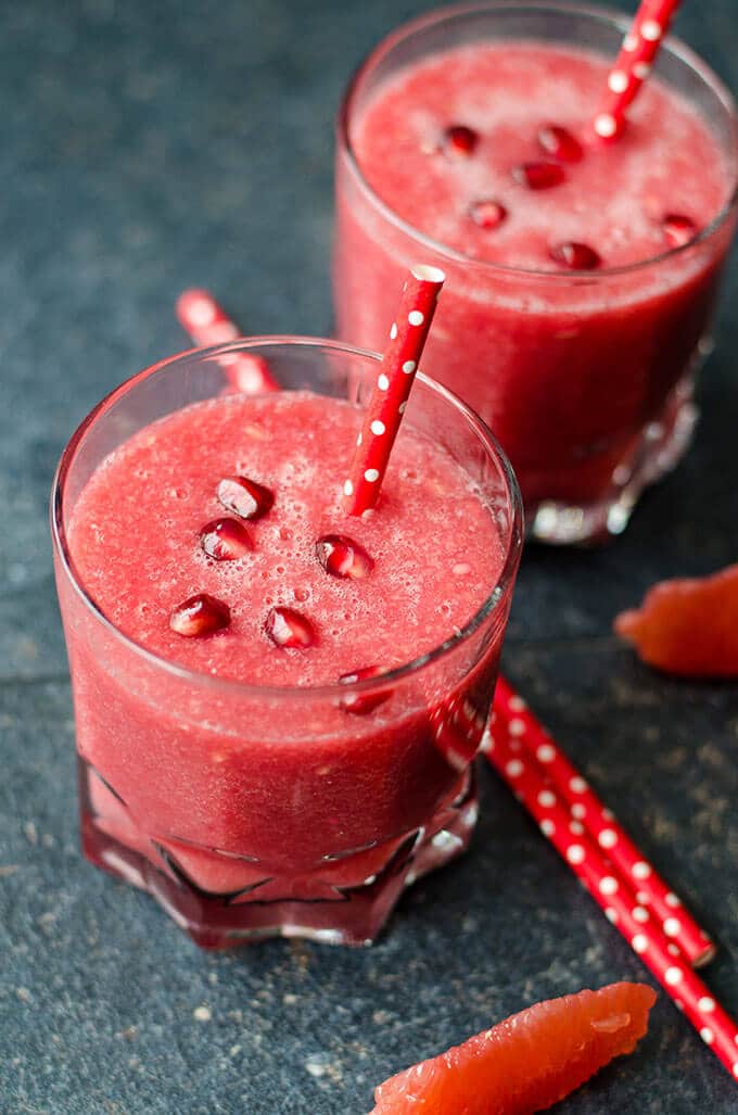Healthy Red Velvet Grapefruit Smoothie is a real immune system booster. Packed with refreshing citrus fruit and pomegranate. No sugar or food coloring is added. Energizes your body. #healthysmoothie #grapefruitsmoothie #valentinesdaybreakfast Healthy grapefruit smoothie garnished with pomegranate arils and red straws.