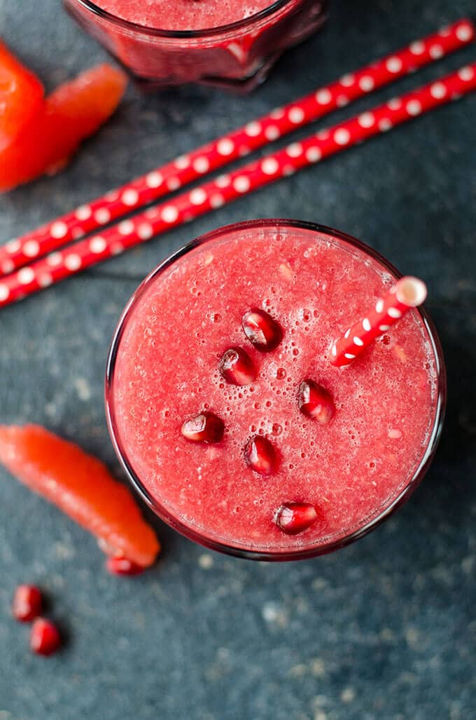 Healthy Red Velvet Grapefruit Smoothie is a real immune system booster. Packed with refreshing citrus fruit and pomegranate. No sugar or food coloring is added. Energizes your body. #healthysmoothie #grapefruitsmoothie #valentinesdaybreakfast Grapefruit juice smoothie garnished with pomegranate arils and red straws on the side