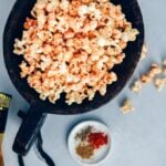 Spicy popcorn served in a large wooden bowl accompanied by spices in a small plate.