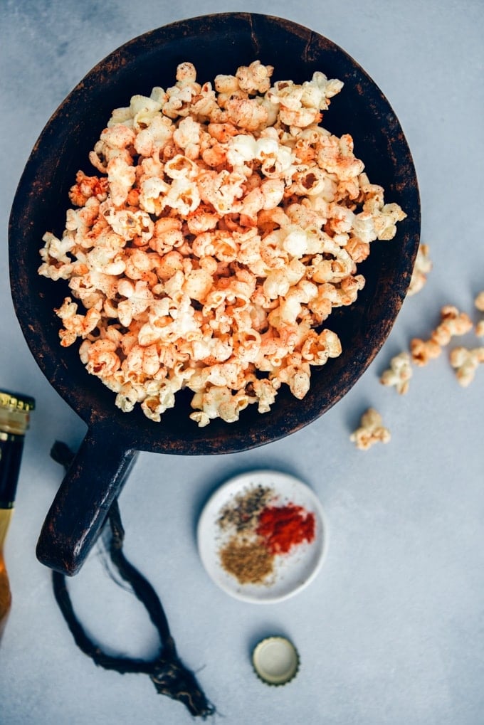 Spicy popcorn served in a large wooden bowl accompanied by spices in a small plate.