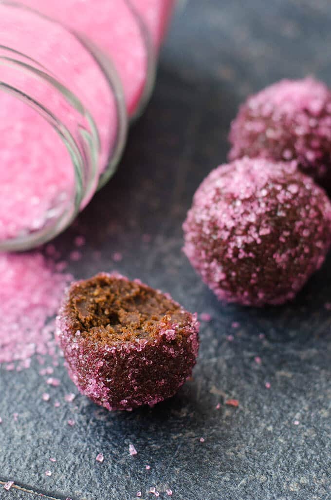 Homemade truffles coated with pink colored sugar on a dark background, one is bitten.