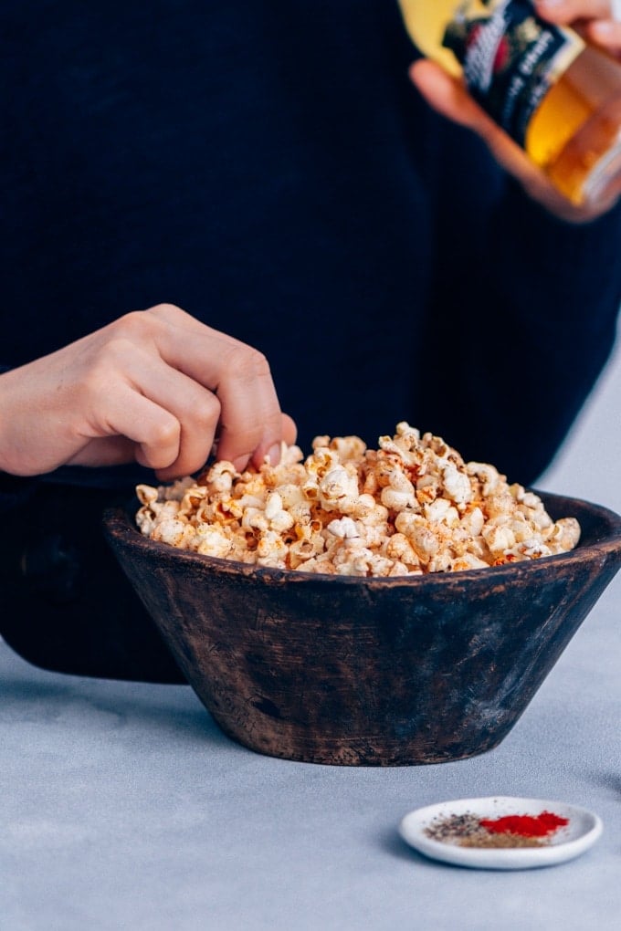 Woman eating spicy popcorn from a bowl and drinking beer.