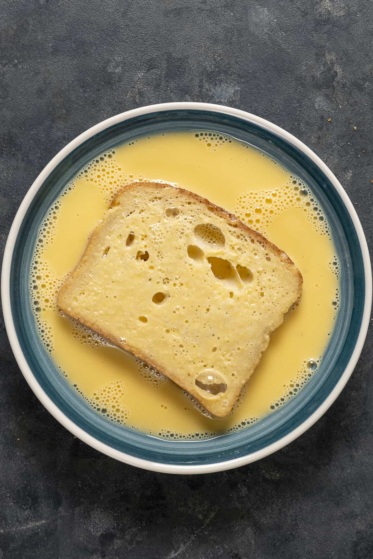 A slice of bread in a mixture of egg and milk in a bowl.