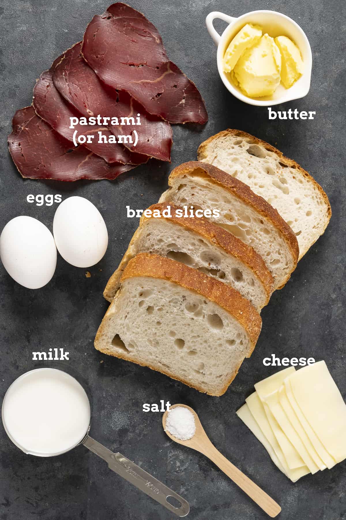 Eggs, cold meat slices, butter, bread slices, cheese lices, milk and salt on a dark background.
