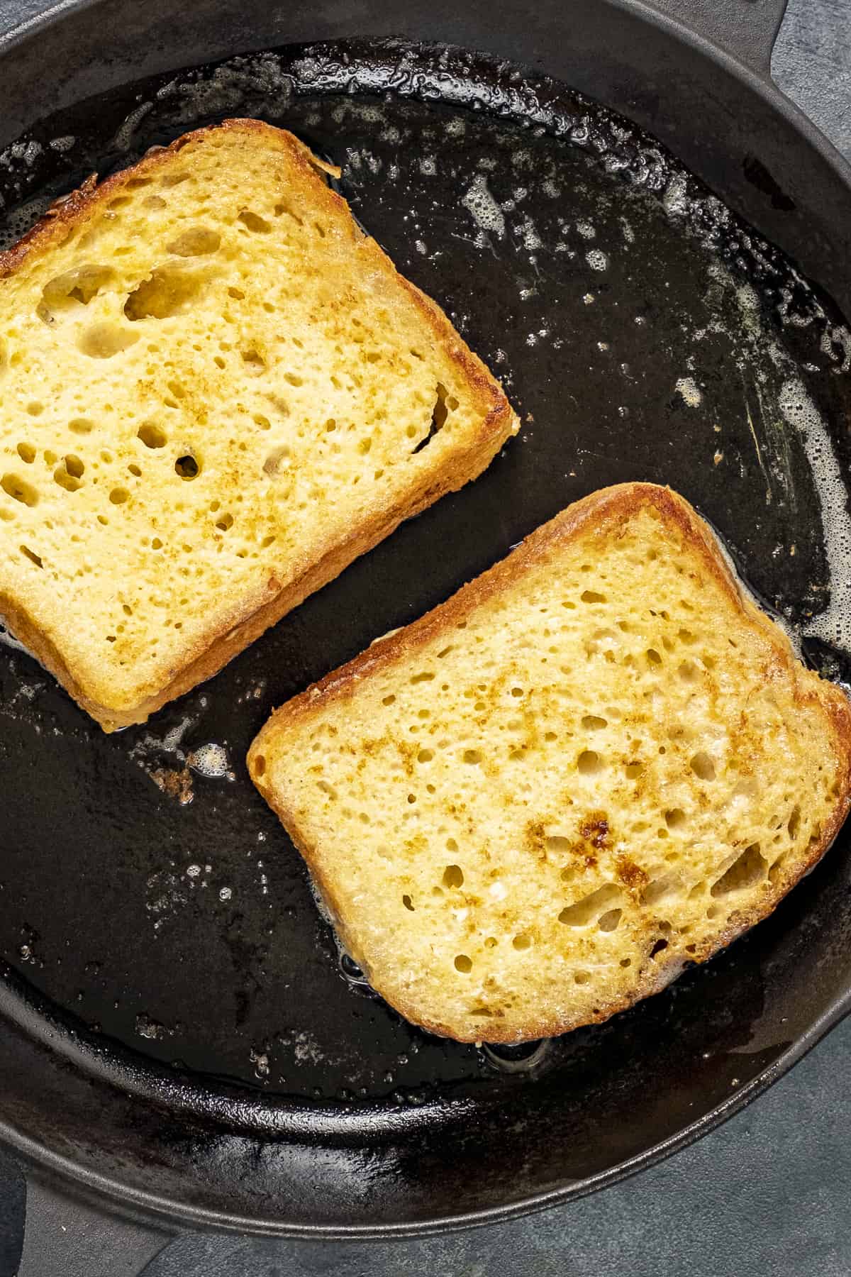 Two slices of bread frying in a non stick pan.