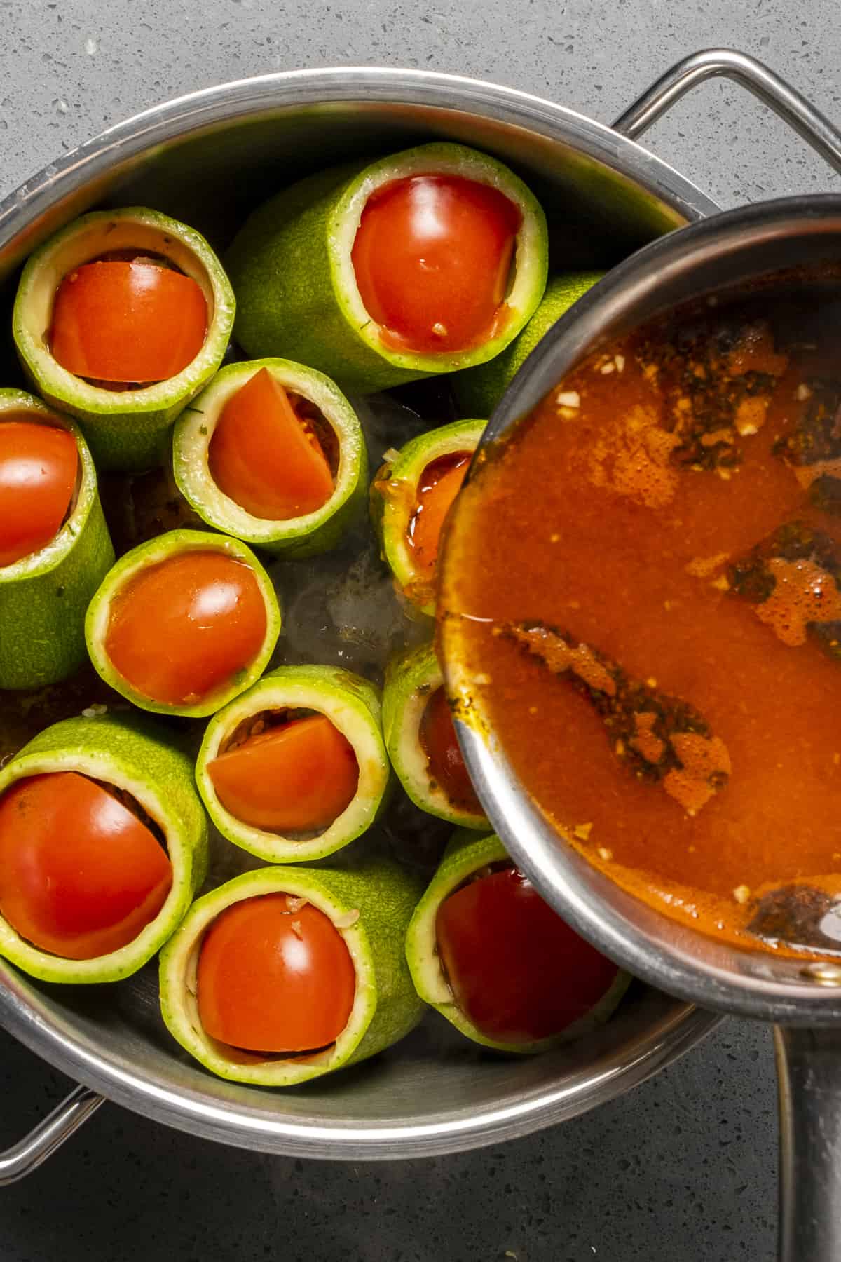 Tomato sauce being poured over stuffed zucchini in a pan.