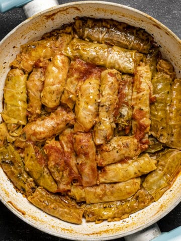 Turkish cabbage rolls with tomato sauce in a white pan.