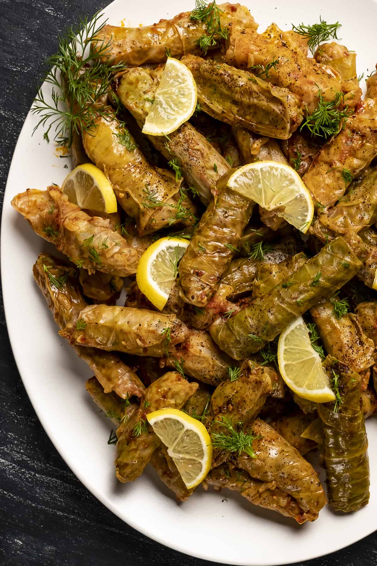 Cabbage rolls garnished with lemon wedges and herbs on a white oval plate.