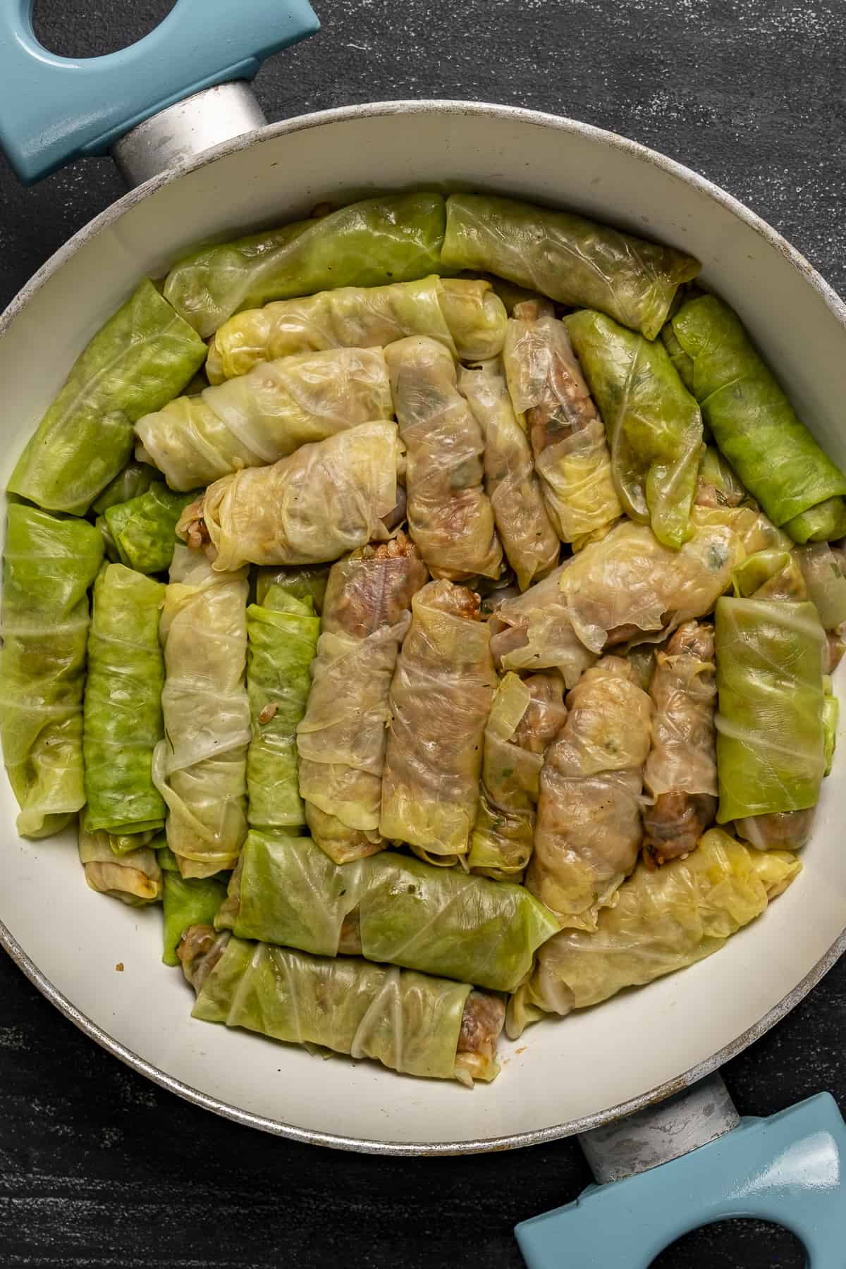 Uncooked cabbage rolls in a white pan.