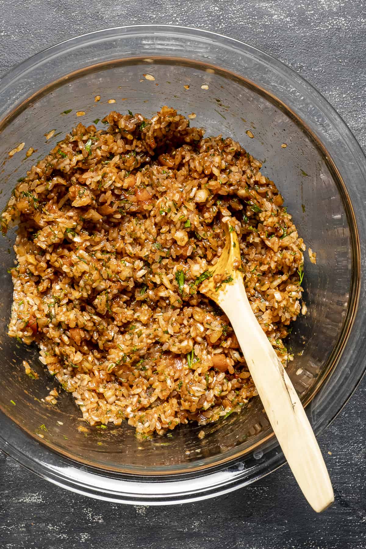 Spiced rice filling for cabbage rolls in a glass bowl and a wooden spoon inside it.