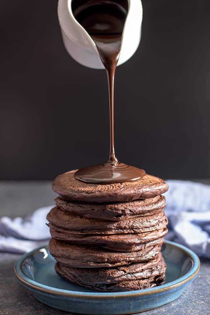 Pouring chocolate ganache on a stack of chocolate chocolate chip pancakes 