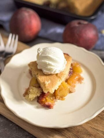 Peach cobbler slice topped with ice cream on a white plate.