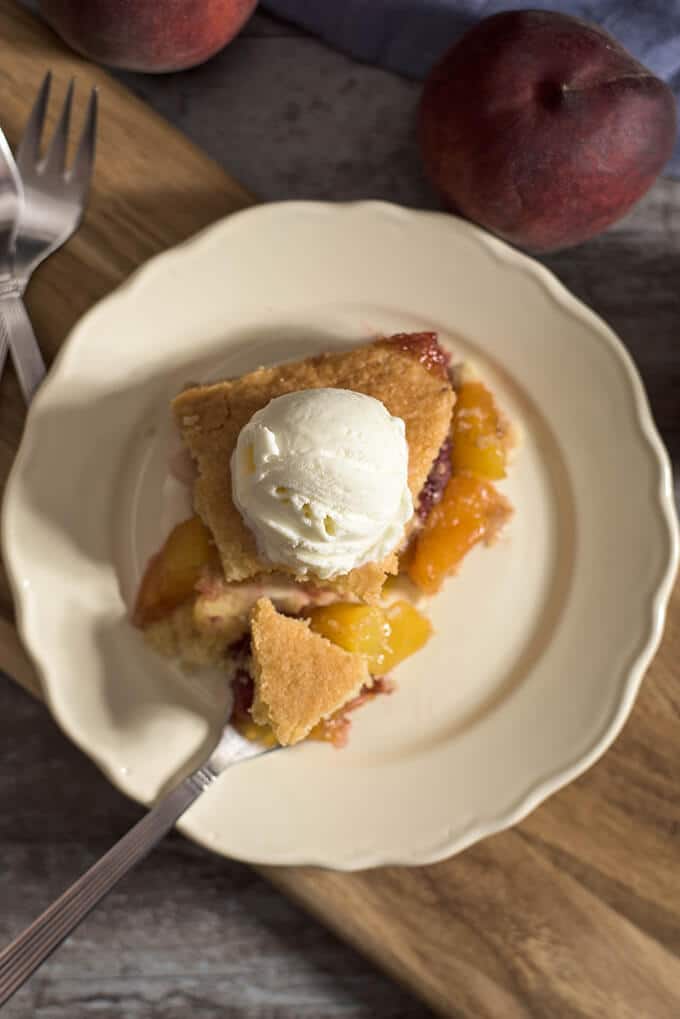 Peach cobbler slice topped with ice cream on a white plate and a fork inside it.