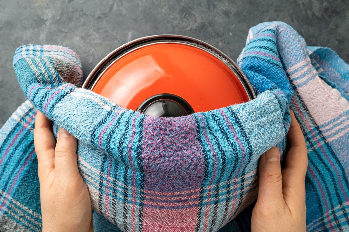 Hands covering the pot of milk and yogurt mixture with a blanket.