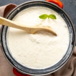 DIY yogurt in an enamel pot with a wooden spoon in it and a sprig of fresh mint on the top.