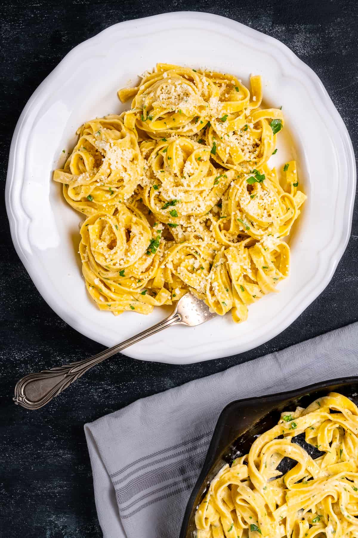 Fettuccine topped with parmesan cheese and chopped parsley in a white bowl and a fork inside it.