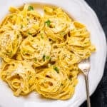 Parmesan cheese pasta in a white bowl and a fork inside it.