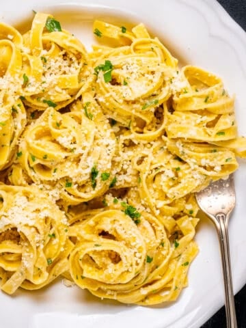 Parmesan cheese pasta in a white bowl and a fork inside it.