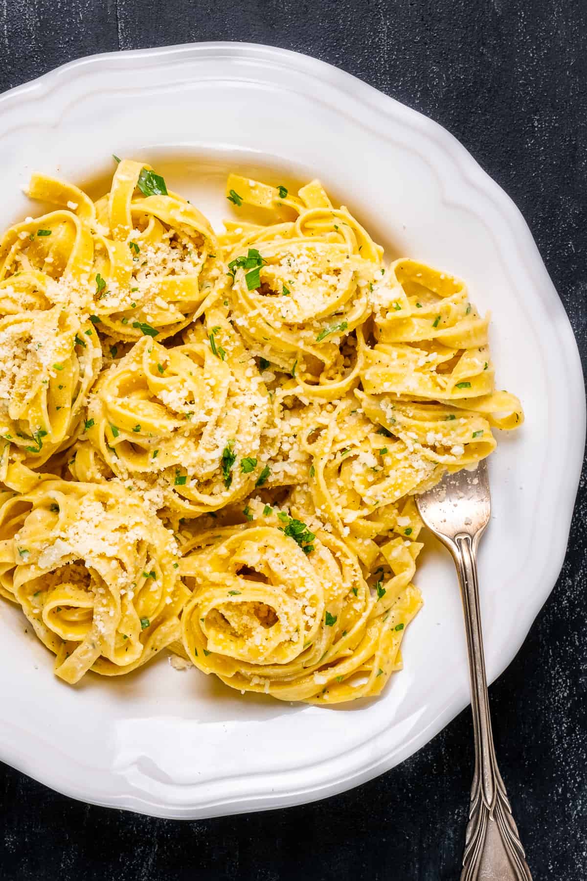 Pasta with parmesan garnished with parsley served in a white bowl and a fork inside it.