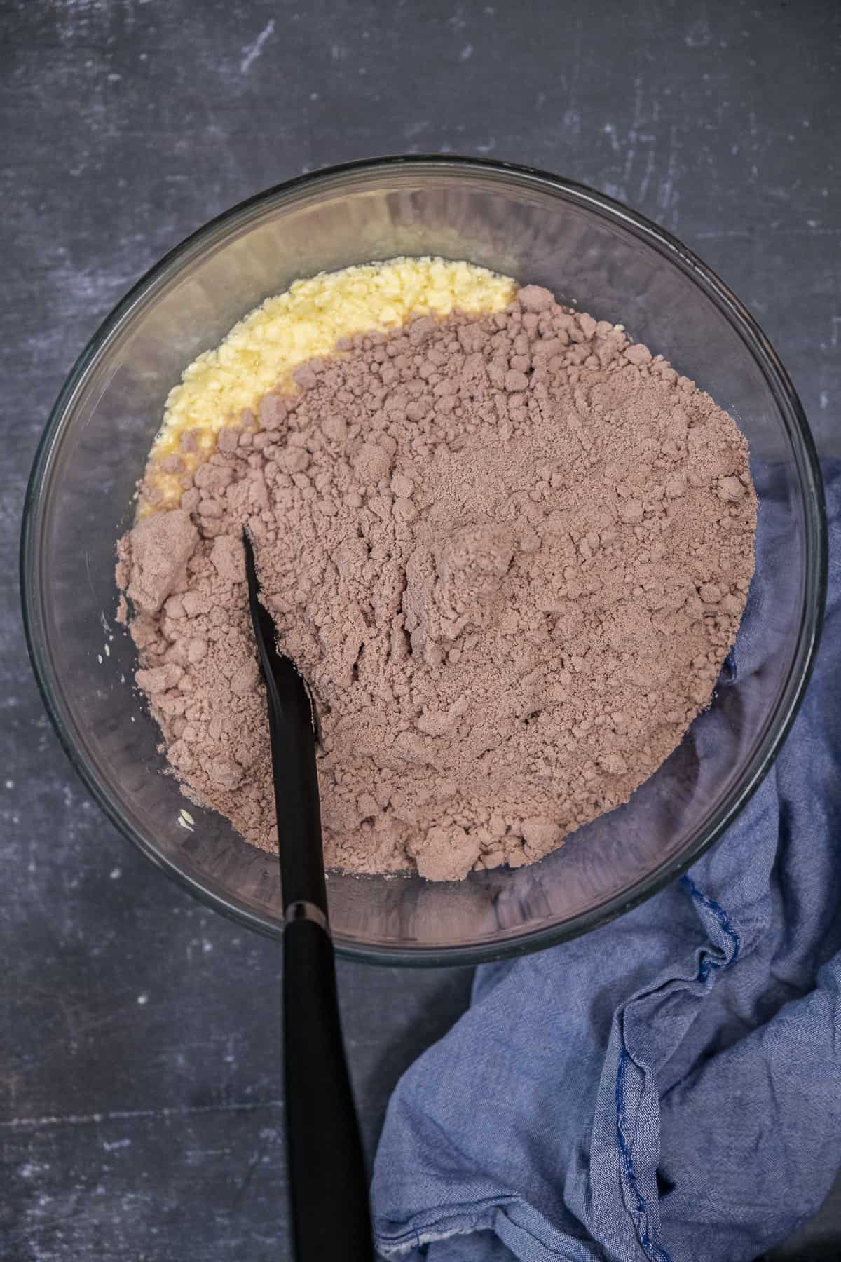 Red velvet cake mix and egg and butter mixture in a glass mixing bowl and a black spatula inside it.
