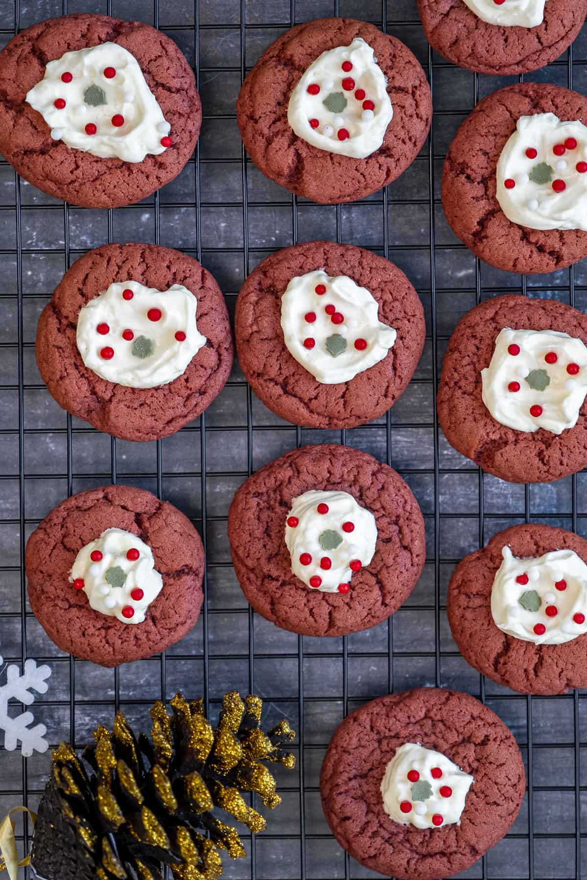 Red velvet cookies topped with cream cheese frosting and decorated with sprinkles on a wire rack.