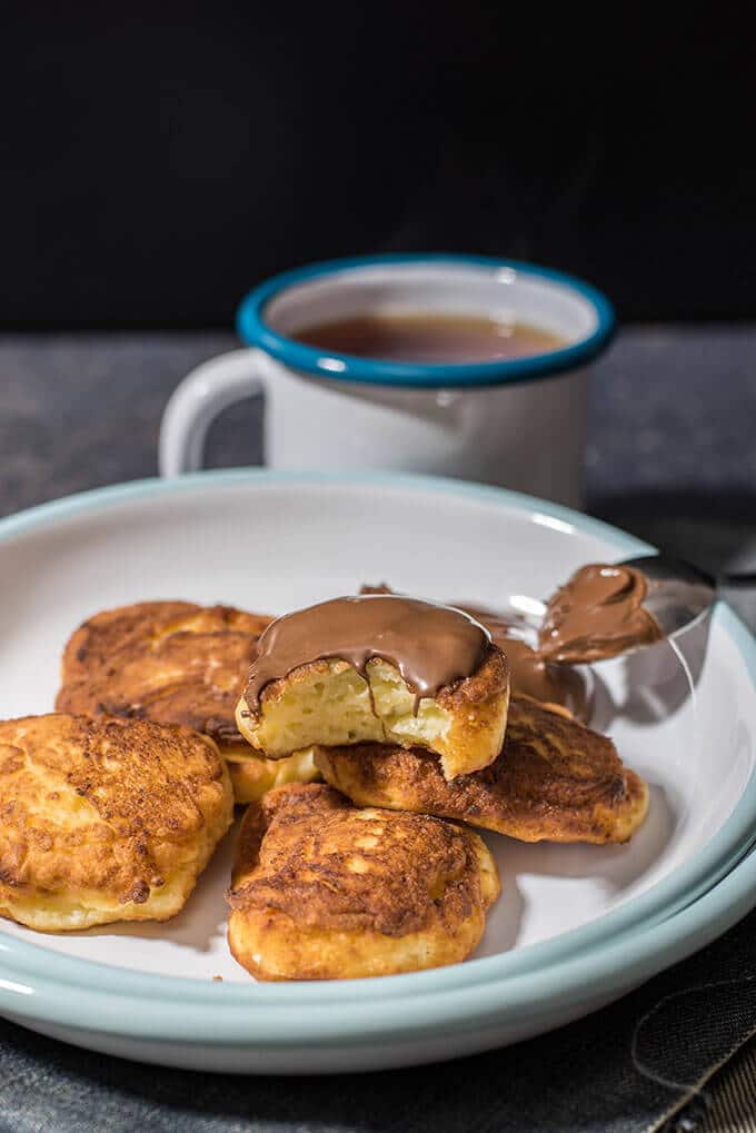 Cheese pancakes on a white plate. One of them is topped with chocolate sauce.