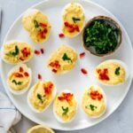 Deviled eggs without mayo garnished with parsley and red bell pepper on a white plate.