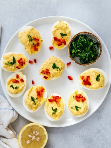 Deviled eggs without mayo garnished with parsley and red bell pepper on a white plate.