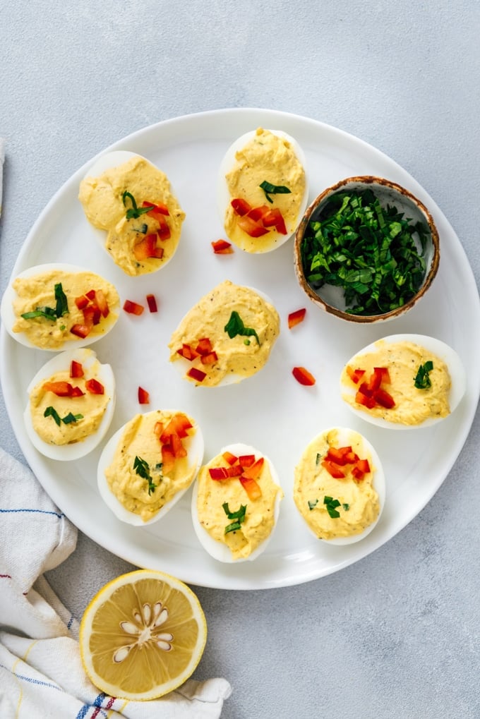 Deviled eggs without mayo garnished with parsley and red bell pepper on a white plate.