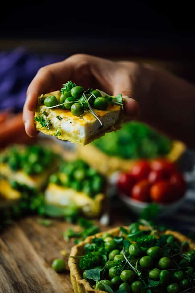 Hand holding a slice of cheese tart with peas and herbs