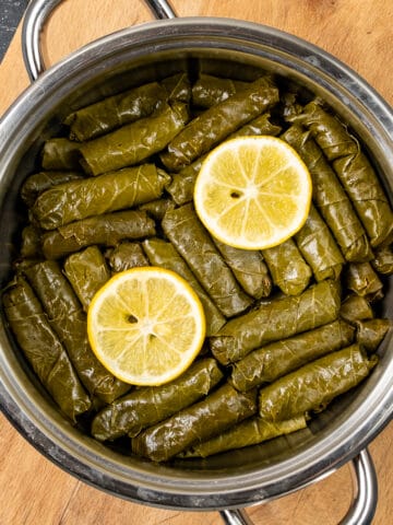 Dolmades with lemon slices on the top in a pot.