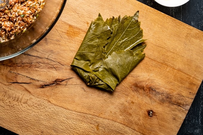 How to stuff grape leaves is shown on a wooden board.