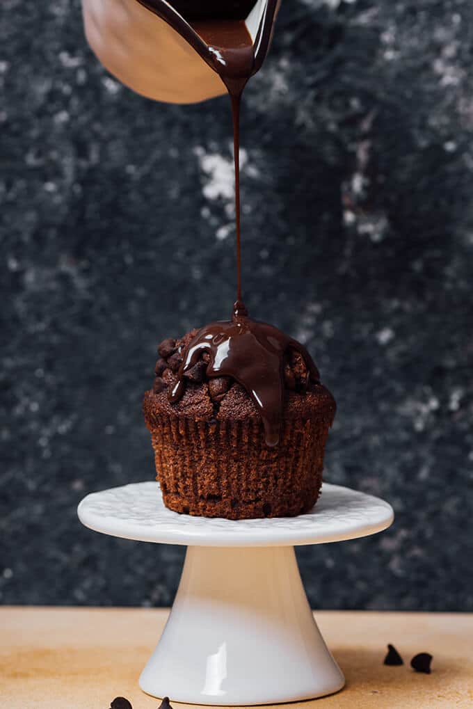 Pouring silky chocolate ganache ove a chocolate muffin.