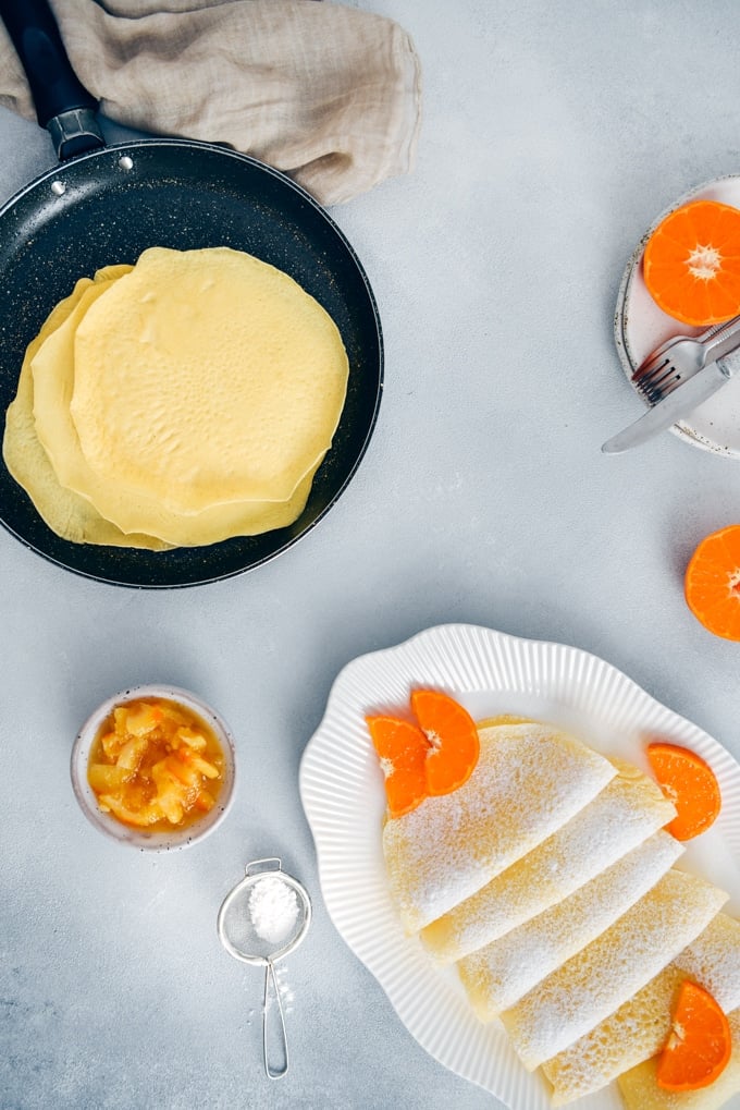 Wonderfully thin gluten free crepes made with rice flour are no different from regular crepes! So easy to make with only 4 simple ingredients. Perfect for several filling options! #glutenfreebreakfast #glutenfreecrepes #riceflourrecipes Rice flour crepes garnished with orange slices and powdered sugar.