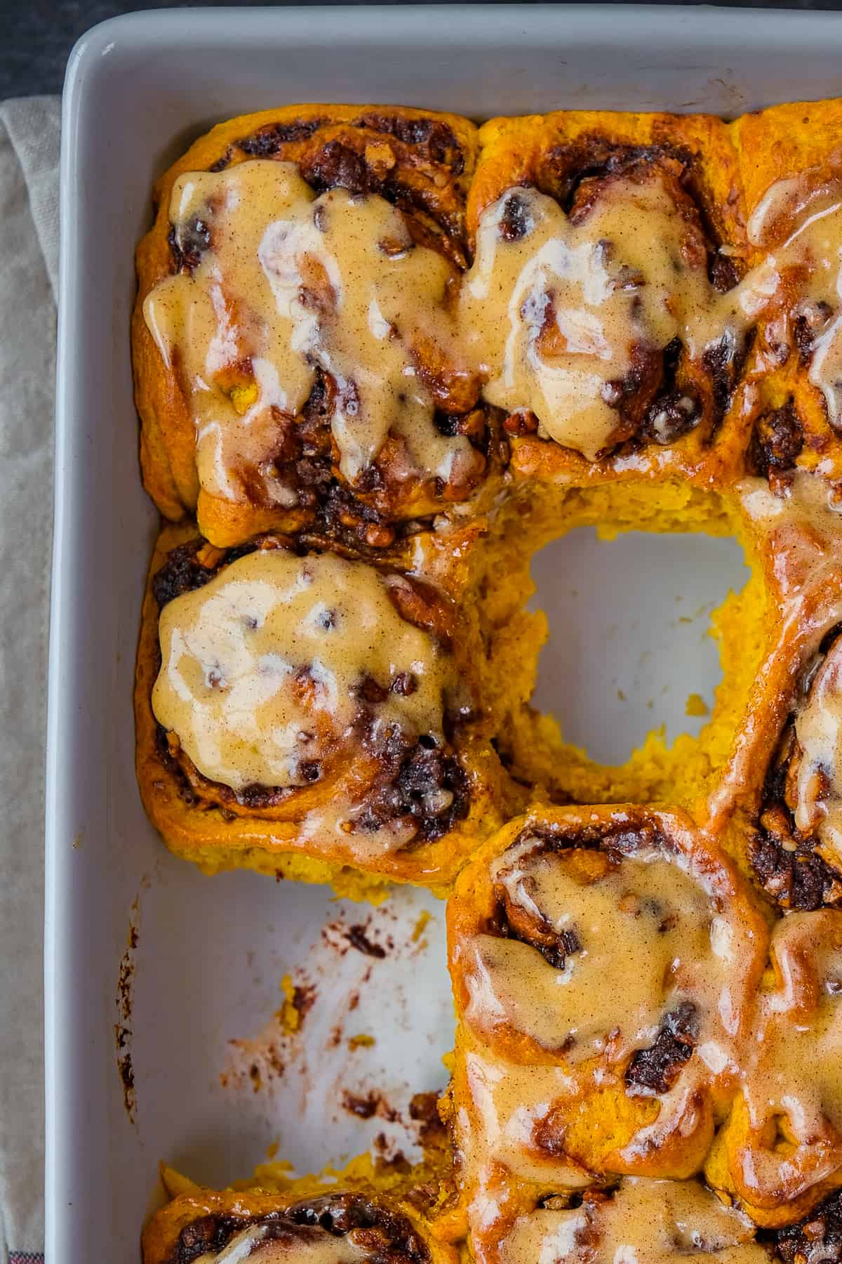 Pumpkin cinnamon rolls frosted with pumpkin spice butter photographed in a pan, two of them are taken.