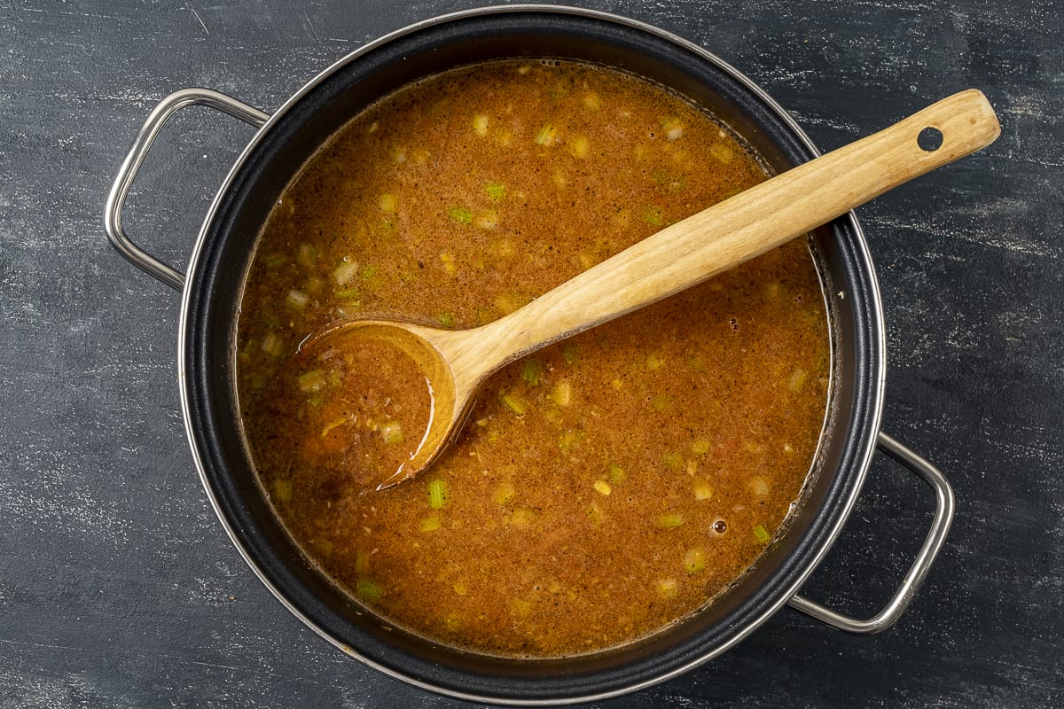 Green lentils and vegetables cooking in a pan and a wooden spoon in it.