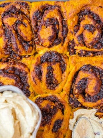 Pumpkin spice frosting being spread on cinnamon pumpkin rolls.