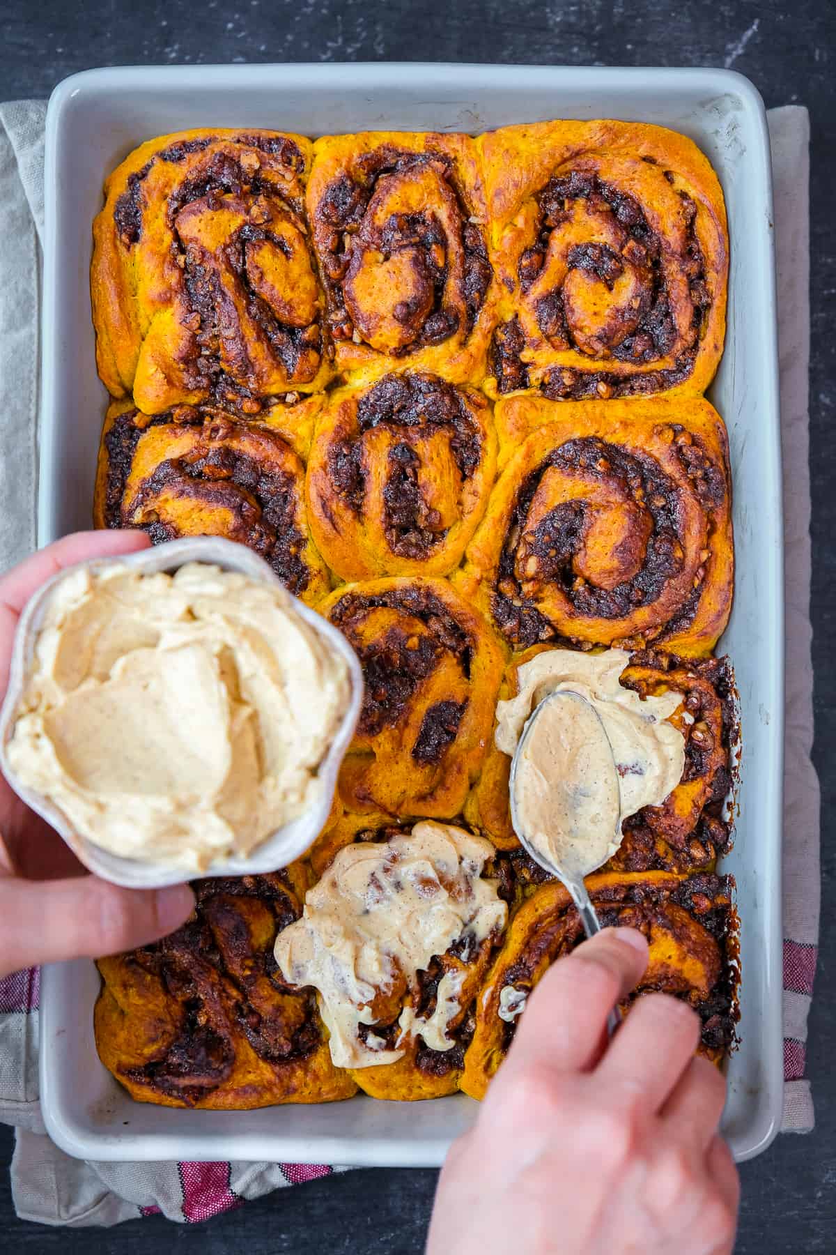 Hands spreading some frosting on pumpkin cinnamon rolls.