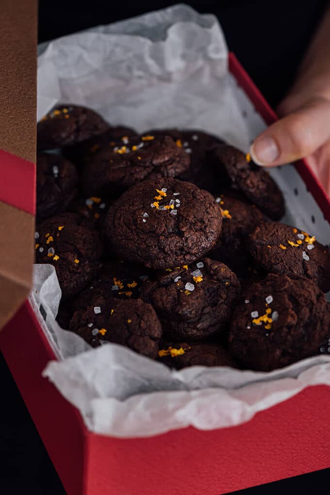 Salted chocolate cookies with orange zest. Woman holding a red gift box that s full of these cookies.