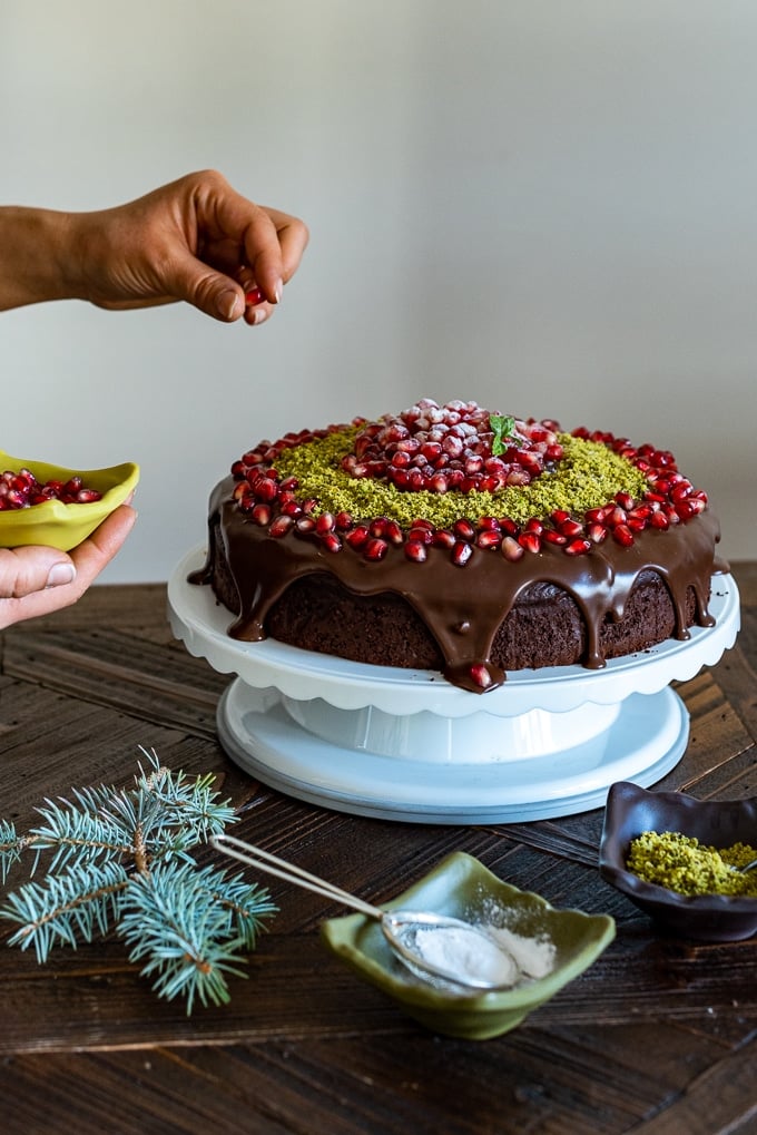 Garnishing chocolate yogurt cake with pomegranate arils and ground pistachio.