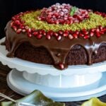 Christmas chocolate cake with ganache, pomegranate seeds and ground pistachio on a cake stand.