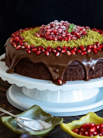 Christmas chocolate cake with ganache, pomegranate seeds and ground pistachio on a cake stand.