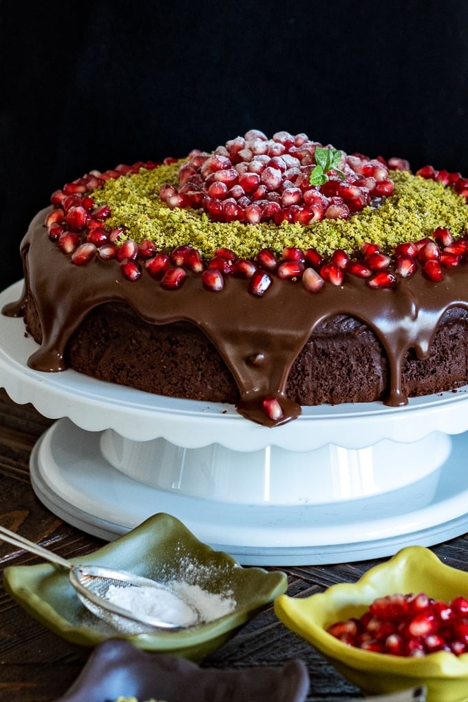 Christmas chocolate cake with ganache, pomegranate seeds and ground pistachio on a cake stand.