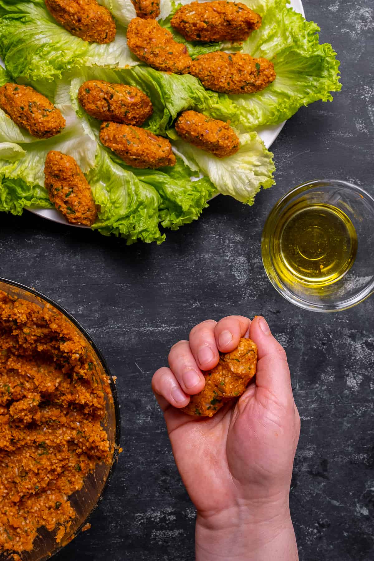 Mercimek koftesi being shaped in a hand, more lentil balls and a small bowl of olive oil on the side.