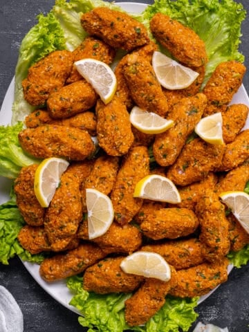 Mercimek kofte served with lettuce leaves and lemon slices on an oval plate.