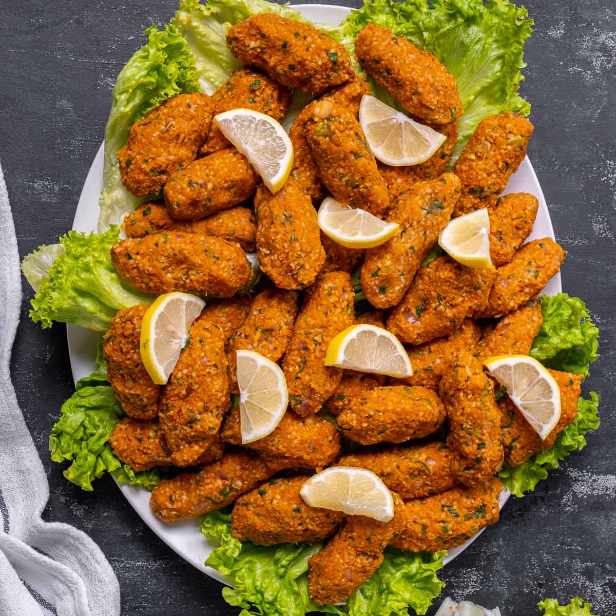 Mercimek kofte served with lettuce leaves and lemon slices on an oval plate.